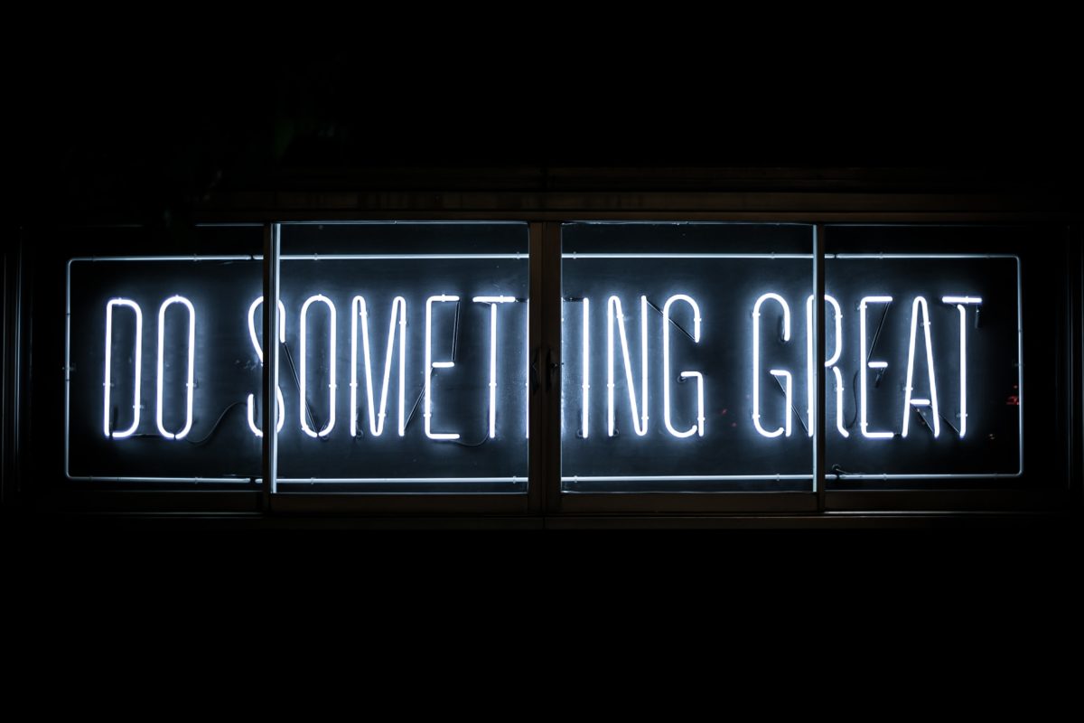 A white lit neon sign on a dark wall saying "Do something great".